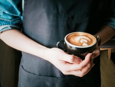 A barista holds a coffee cup with beautiful latte art in a cozy café setting.